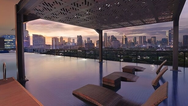 An infinity pool with wicker loungers and a city skyline view. - Samara Suites by Emily in Jakarta (Jakarta)