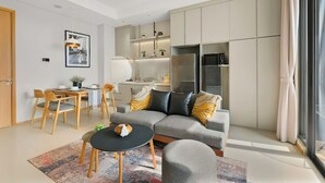 A modern living room with a grey sofa, a small round table, and a dining area with wooden chairs. - Samara Suites by Emily in Jakarta (Jakarta)