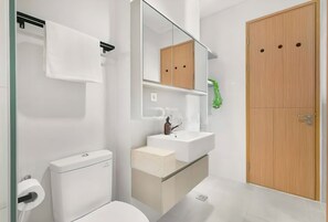 Bathroom features a toilet, sink, and mirror, with a small plant nearby.