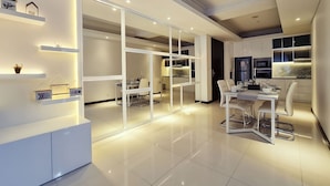 A modern kitchen with white cabinetry, a dining area with a glass partition, and a built-in oven. - Casa Grande Residence (Jakarta)