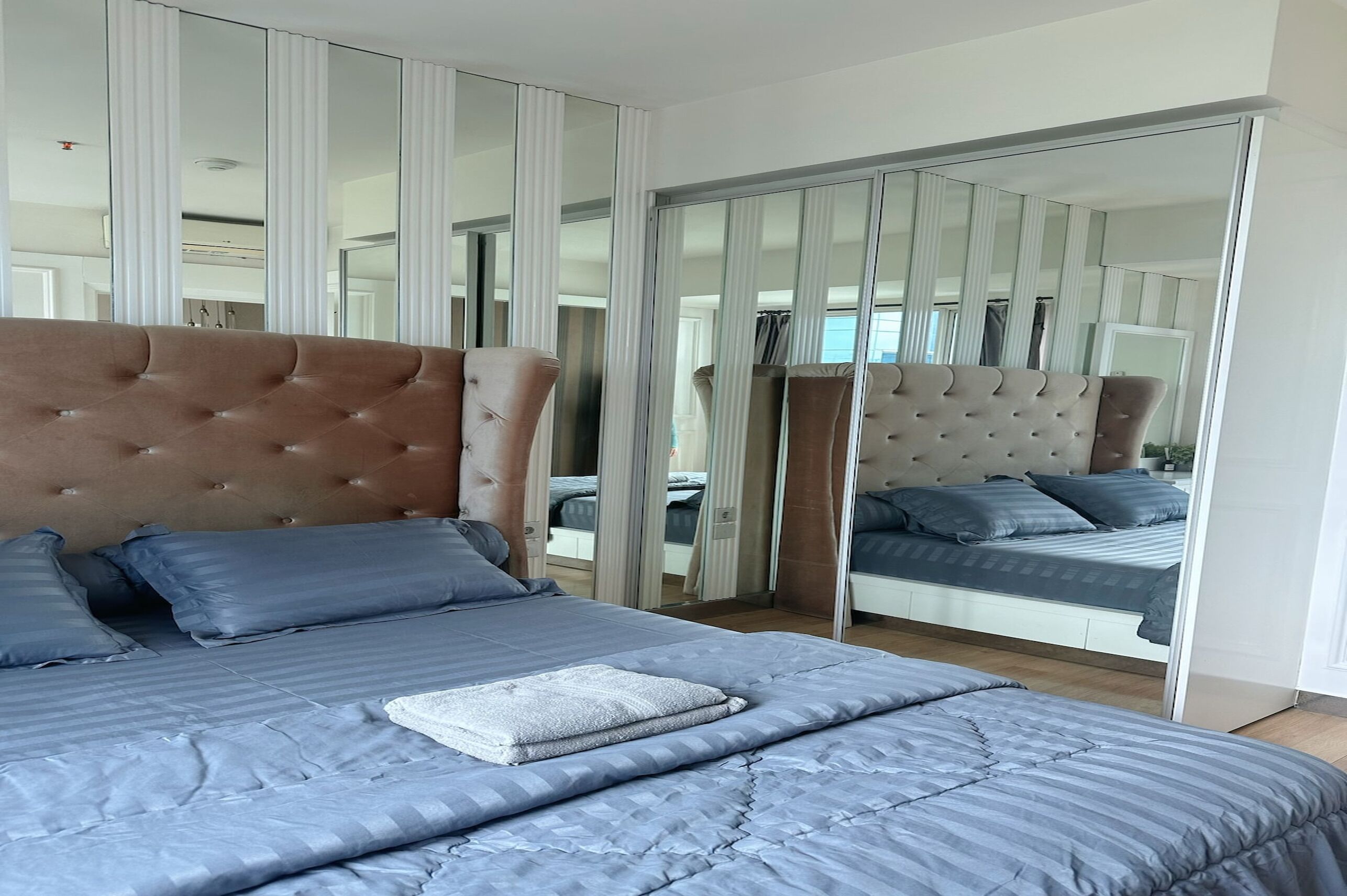A modern bedroom with a large bed, mirrored closet doors, and a view of another room.