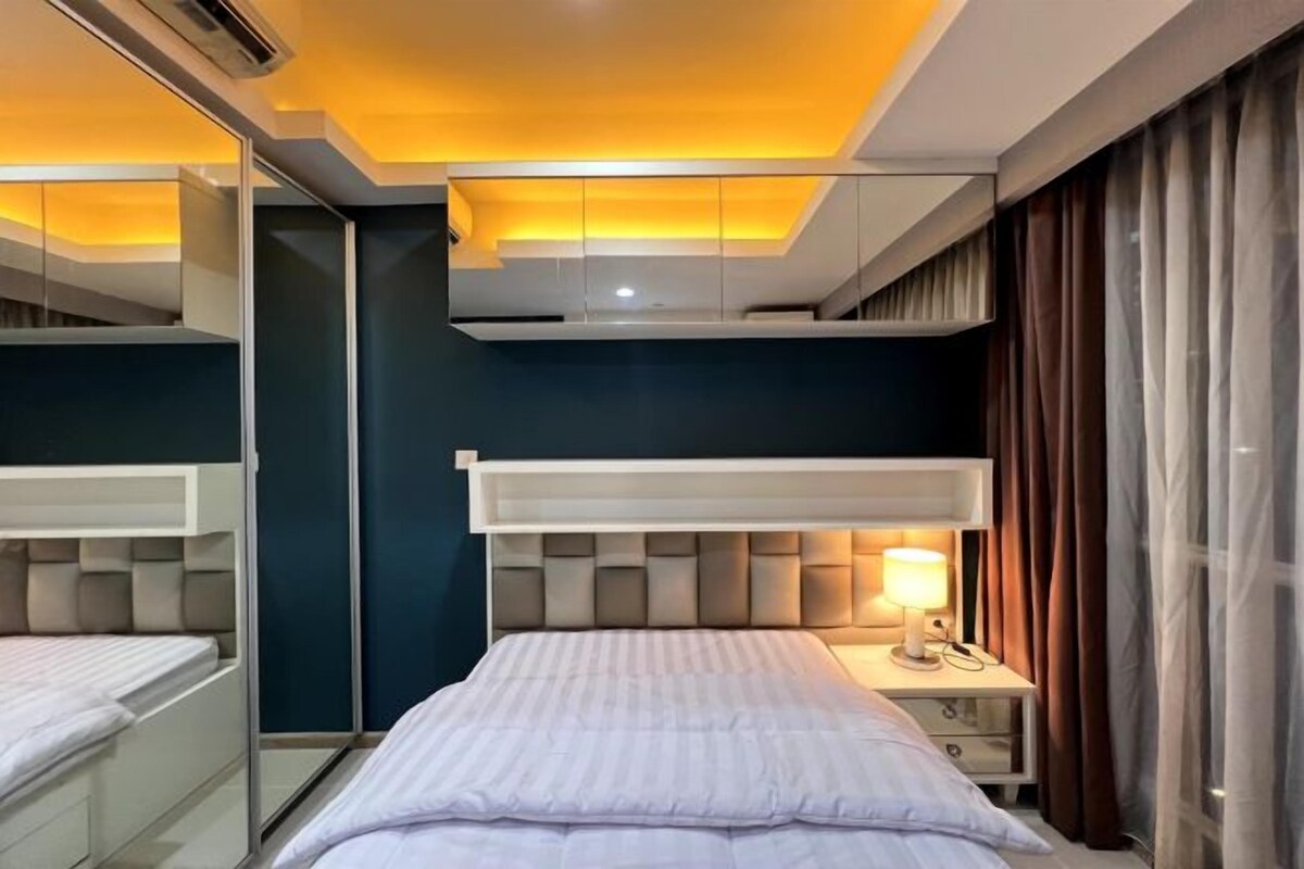 A modern hotel room with a bed, bedside table, lamp, and a mirror.