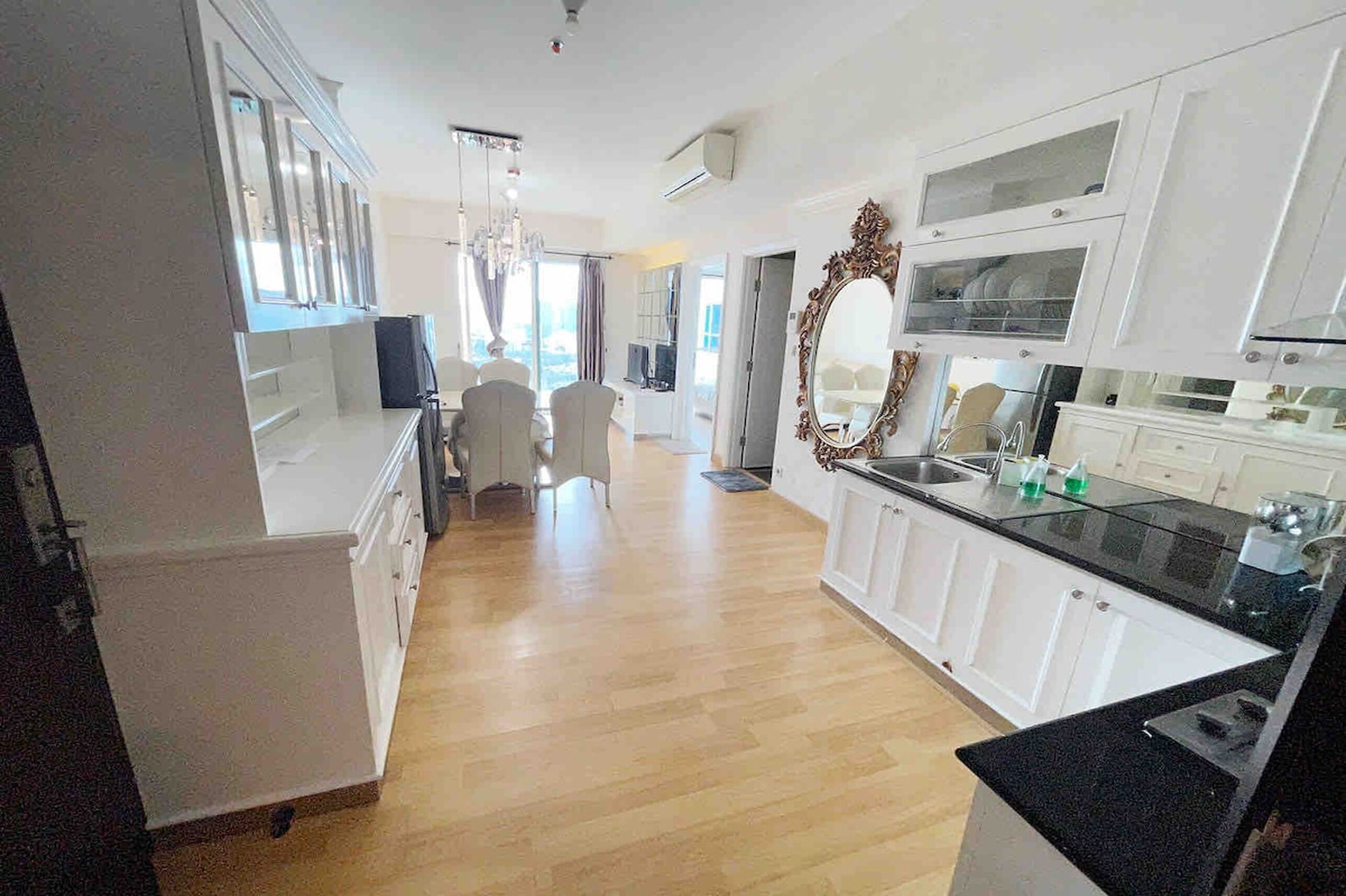 A modern kitchen with white cabinetry, a black countertop, and a large ornate mirror.