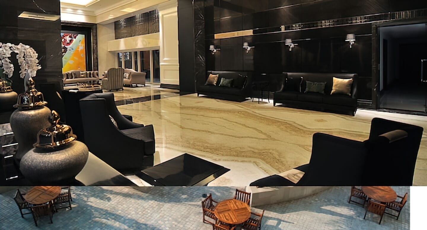 A spacious lobby with a marble floor, black sofas, and a dining area with wooden tables and chairs.