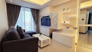 A modern living room with a sofa, coffee table, and a TV mounted on a marble wall. - Casa Grande Residence (Jakarta)