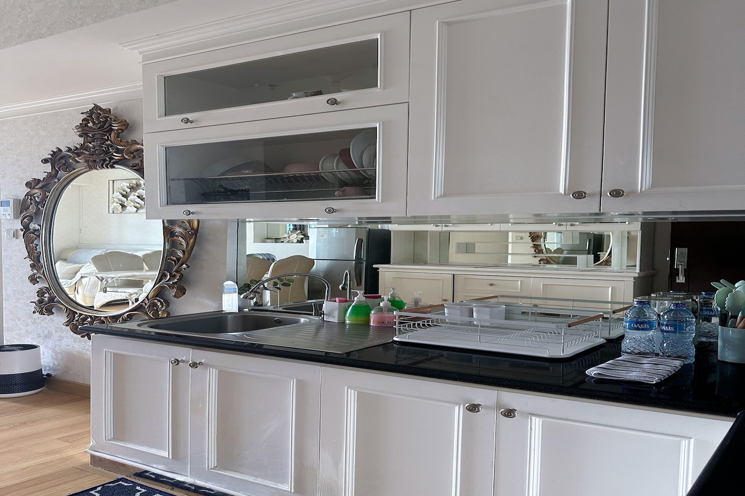 A kitchen with white cabinets, a black countertop, and a large ornate mirror.