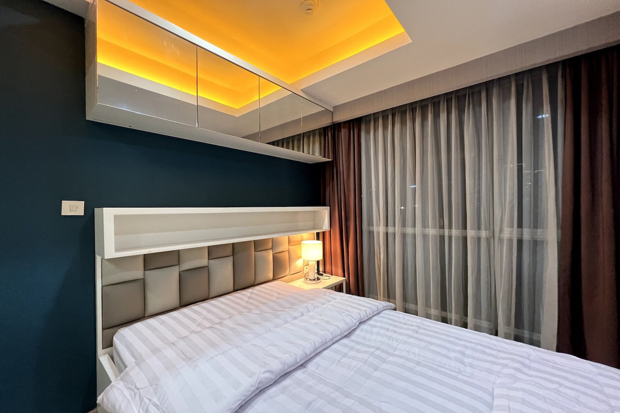 Ein modernes Hotelzimmer mit Bett, Nachttisch und einem großen Fenster mit Vorhängen.