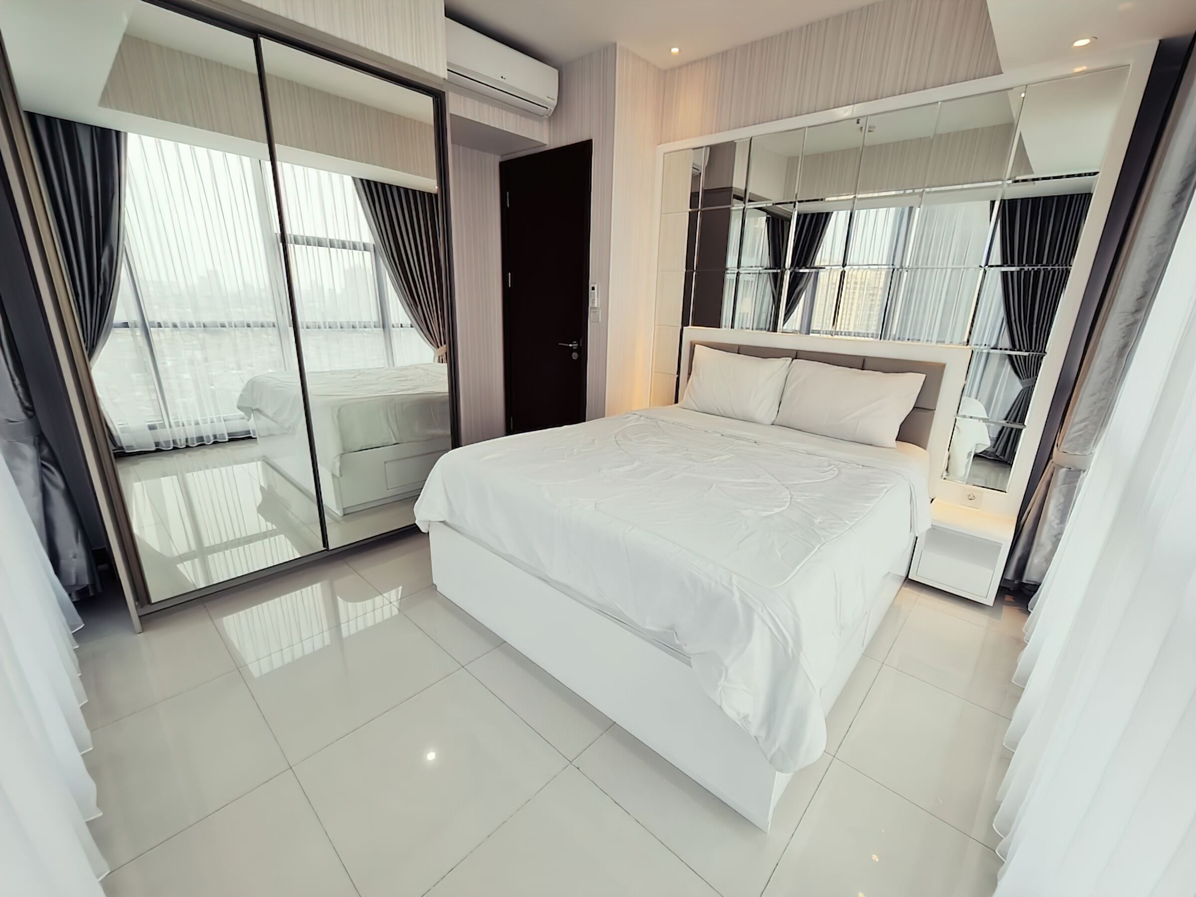 A modern hotel room with a large bed, a sliding glass door leading to a balcony, and a built-in wardrobe with mirrors.