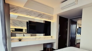 A modern hotel room with a marble-patterned ceiling, a large flat-screen TV, a white vanity with a mirror, and a bed with white bedding. - Casa Grande Residence (Jakarta)