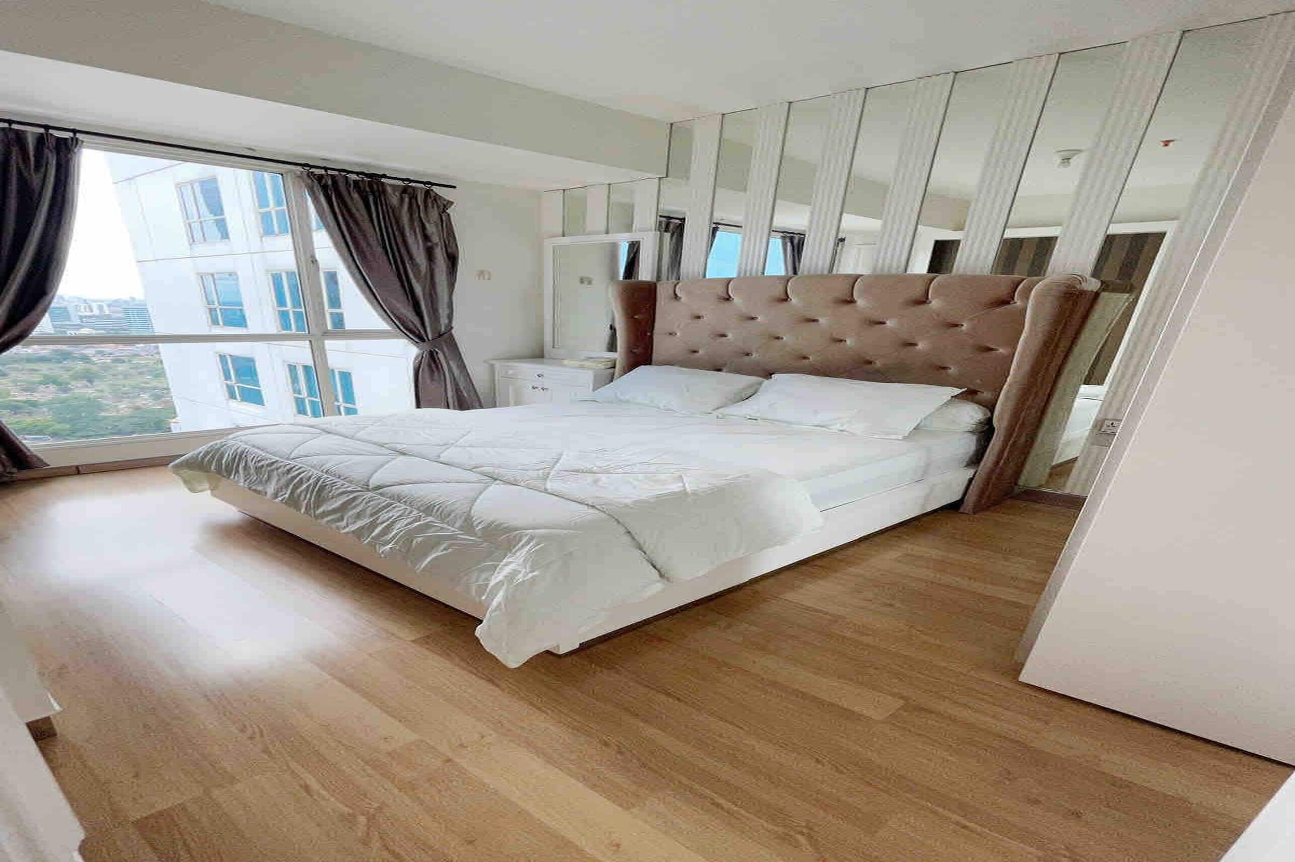Een slaapkamer met een groot bed, een nachtkastje, een spiegel en een raam met gordijnen.