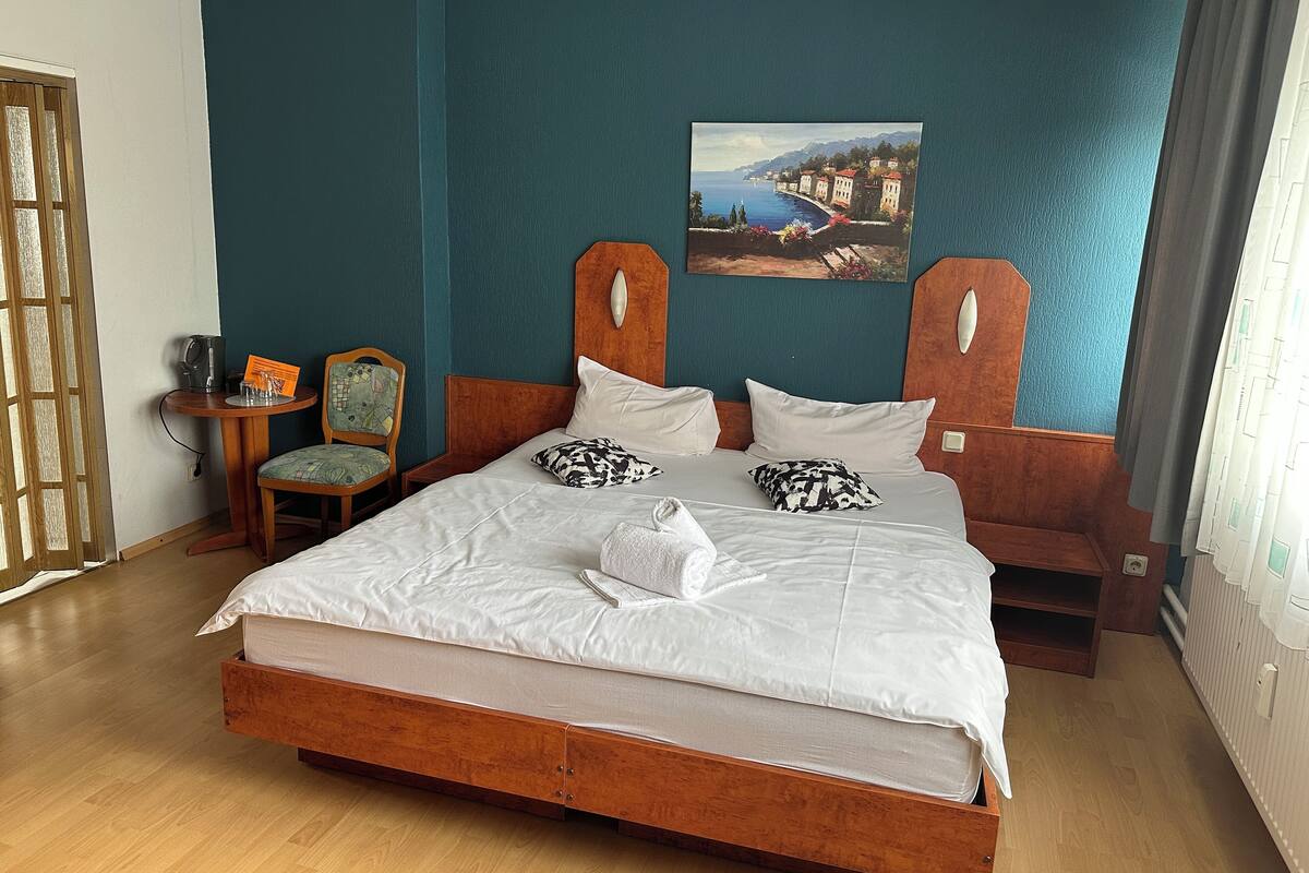 A bedroom with a wooden bed, teal walls, a painting, and a chair.