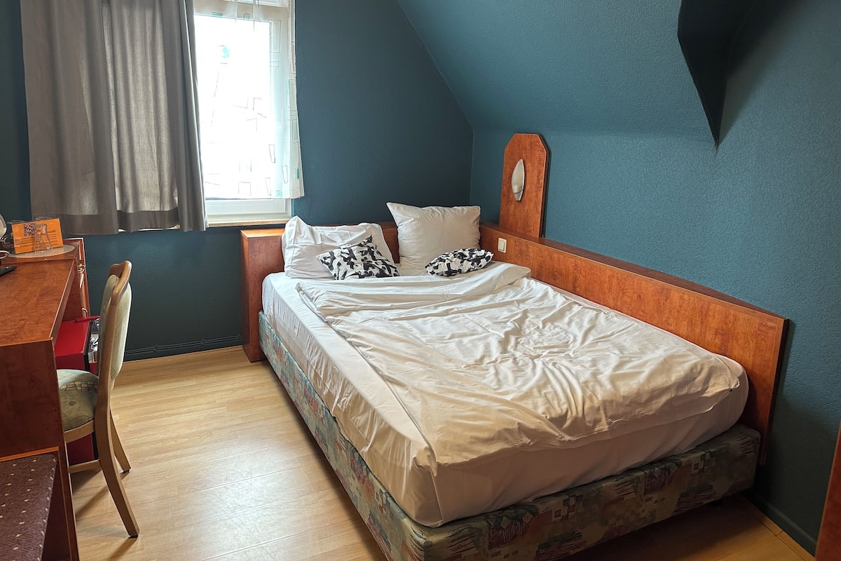A bedroom with a bed, a desk, a chair, and a window with curtains.