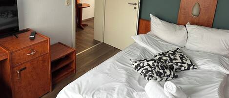 Habitación de hotel con cama, televisor, mesita de noche de madera y puerta que da a un baño.