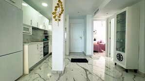 A modern kitchen with white cabinets, a marble floor, and a black rug leading to a bedroom with a pink bed.