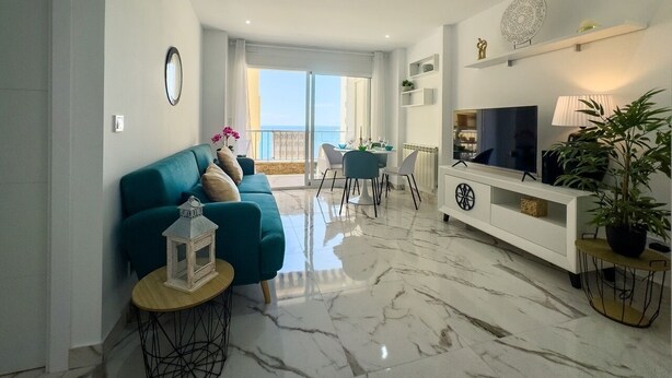 A modern living room with a teal sofa, a white entertainment unit, and a dining area with a table and chairs.