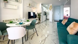 A modern living room with a dining area, a kitchen in the background, and a sofa with cushions.