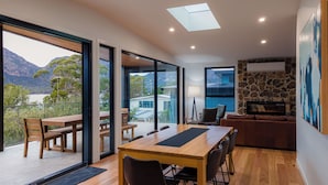 Ein modernes Interieur mit Essbereich, Kamin aus Stein und großen Glastüren, die auf einen Balkon mit Bergblick führen.