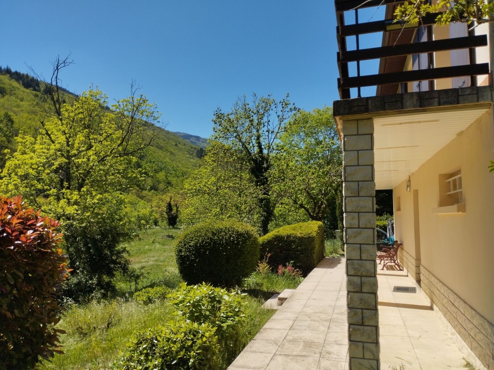 A gated entrance with a stone wall, a small window, and a view of lush greenery and a clear blue sky.