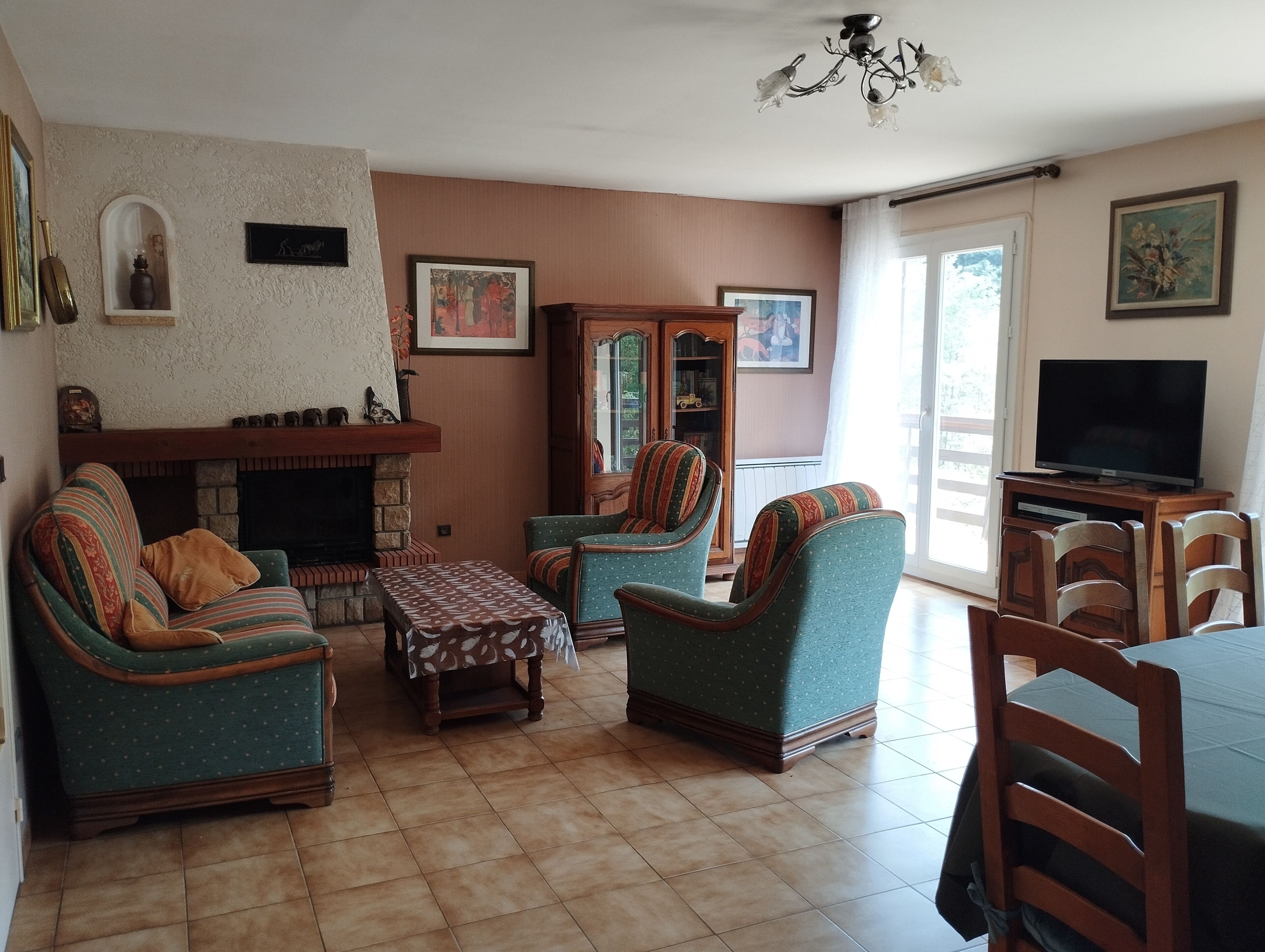 A living room with a fireplace, patterned sofa, armchairs, a small table, and a television.