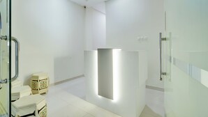 A modern bathroom with a glass shower enclosure, a white toilet, and a small decorative stool. - Hotel O Krekot Residence Pasar Baru (Jakarta)