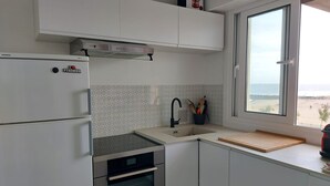 Una cocina moderna con armarios blancos, horno empotrado, campana extractora de acero inoxidable y ventana con vistas a la playa.