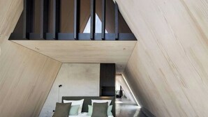 Une chambre moderne de forme triangulaire, dotée d’un lit et d’une lucarne.