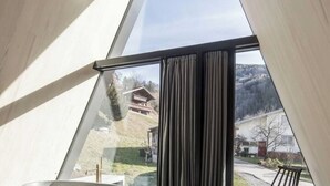 Une pièce dotée d’une grande fenêtre, offrant une vue sur une montagne, et dont l’extérieur est constitué d’une structure en bois.
