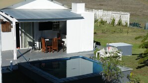 Una casa moderna con piscina, un comedor con sillas y una mesa, y un patio cercado.
