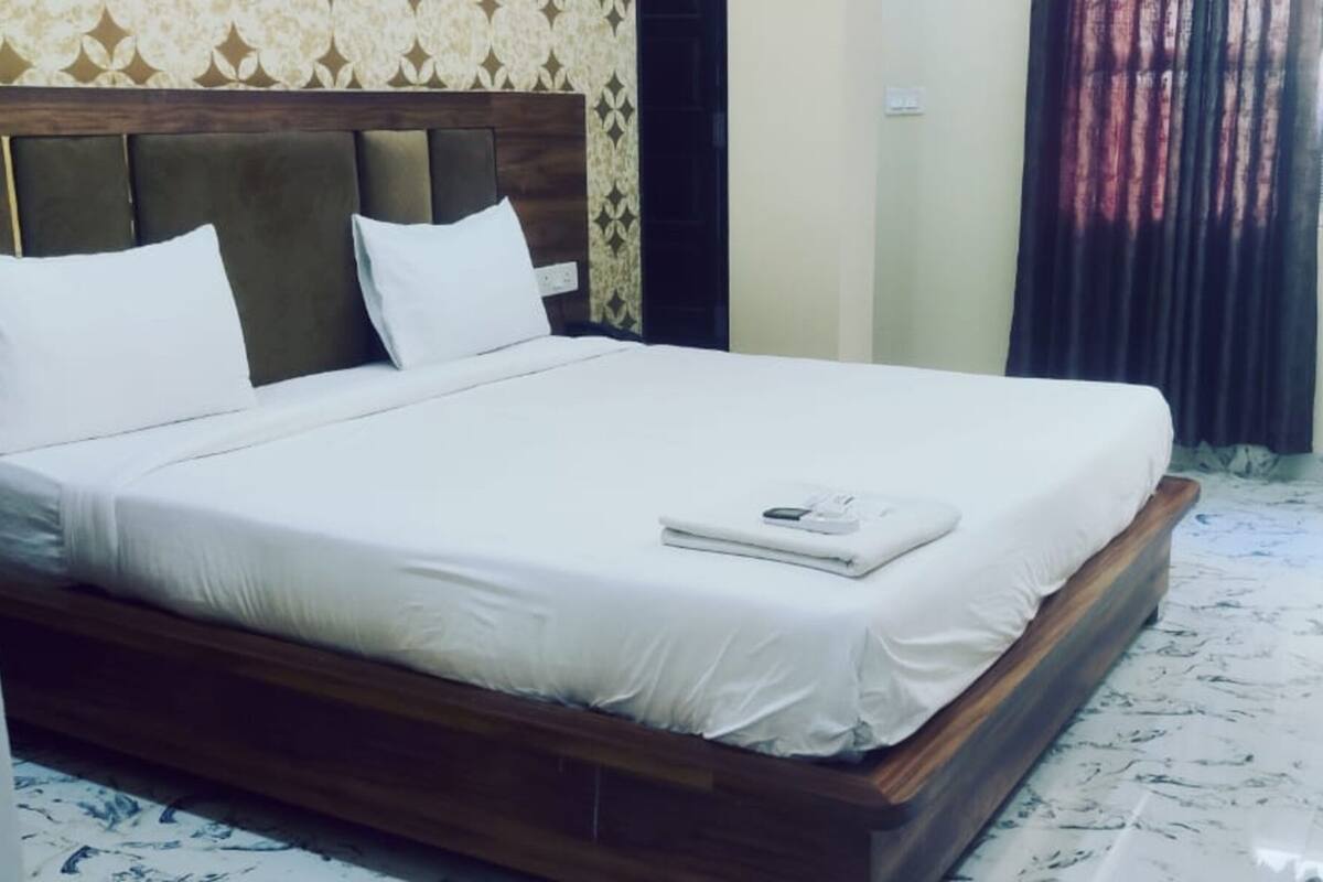 Una cama bien hecha con sábanas blancas, cabecera de madera y una mesita de noche con lámpara.