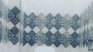 Une petite salle de bain avec des toilettes blanches, des murs carrelés avec un motif en losanges et un seau rouge posé sur le sol.