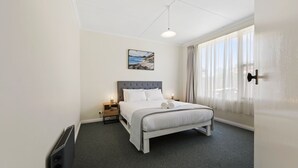 Ein Hotelzimmer mit Bett, Nachttisch, Lampe, einem Bild an der Wand und einem Fenster mit Vorhängen.