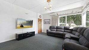 Ein Wohnzimmer mit einem großen Flachbildfernseher, einem dunkelbraunen Ledersofa, einer schwarzen Unterhaltungsanlage und einem Fenster mit Vorhängen.