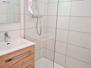A bathroom with a white sink, wooden vanity, and a shower with a handheld showerhead.