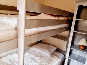 Une chambre avec un lit superposé et une étagère où se trouve une lampe.