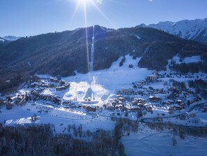 Une station de montagne enneigée, avec plusieurs bâtiments, des pistes de ski et un ciel dégagé.