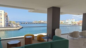 Un balcón con asientos, vistas a un puerto deportivo y edificios al fondo.