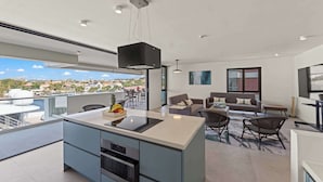 Un apartamento moderno con cocina, comedor y sala de estar. Cuenta con un amplio ventanal con vistas a la ciudad, un balcón y un televisor de pantalla plana.