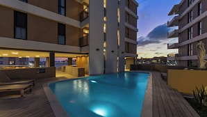 Un hotel moderno con piscina en la azotea, zona de estar al aire libre y vistas a la ciudad al atardecer.