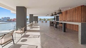 Amplio espacio al aire libre con bar y asientos, con vistas a un cuerpo de agua y al paisaje urbano.