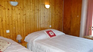 Habitació amb dos llits, parets de fusta, una taula de nit amb una làmpada i una porta.