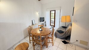 Un salon chaleureux avec une table à manger ronde en bois, deux chaises en bois, un canapé gris, un téléviseur et une lampe.