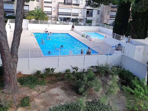 A swimming pool area with multiple pools, surrounded by a white wall and trees.