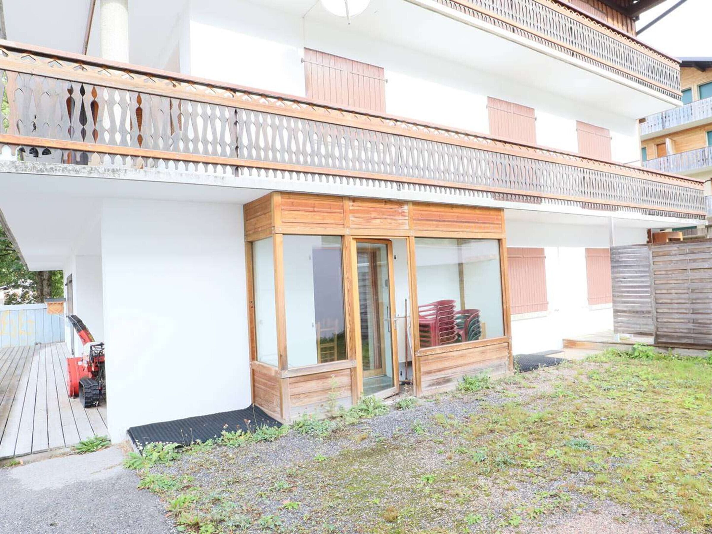 Ein zweistöckiges Gebäude mit Balkon, Holztür und einem kleinen, abgeschlossenen Bereich mit Glastür.