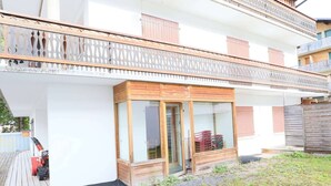 Un bâtiment à deux étages doté d’un balcon, d’une porte en bois et d’un petit espace clos avec une porte en verre.