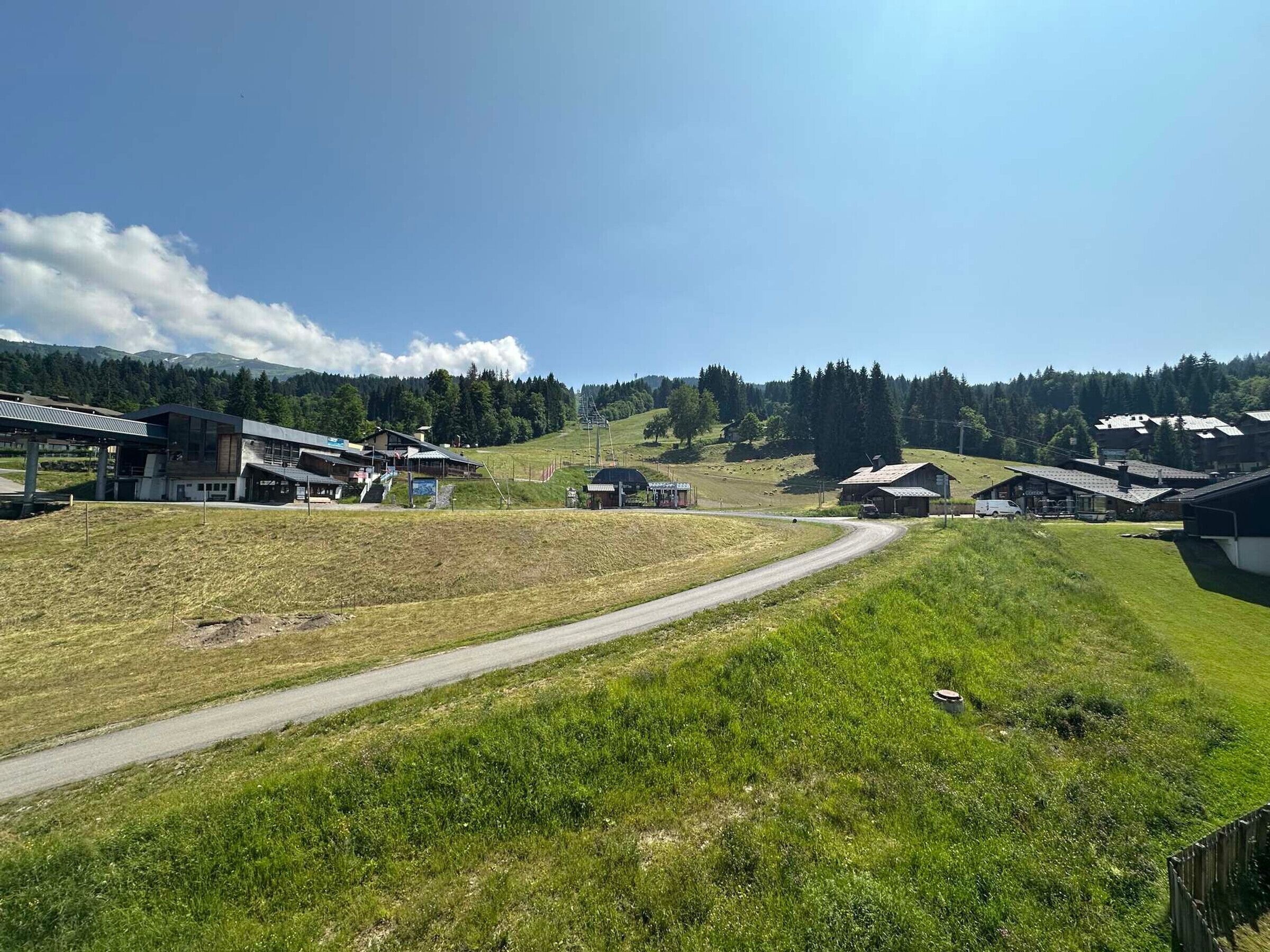 A rural landscape with a road leading to a cluster of buildings, including a modern structure with a sloped roof and a traditional barn.