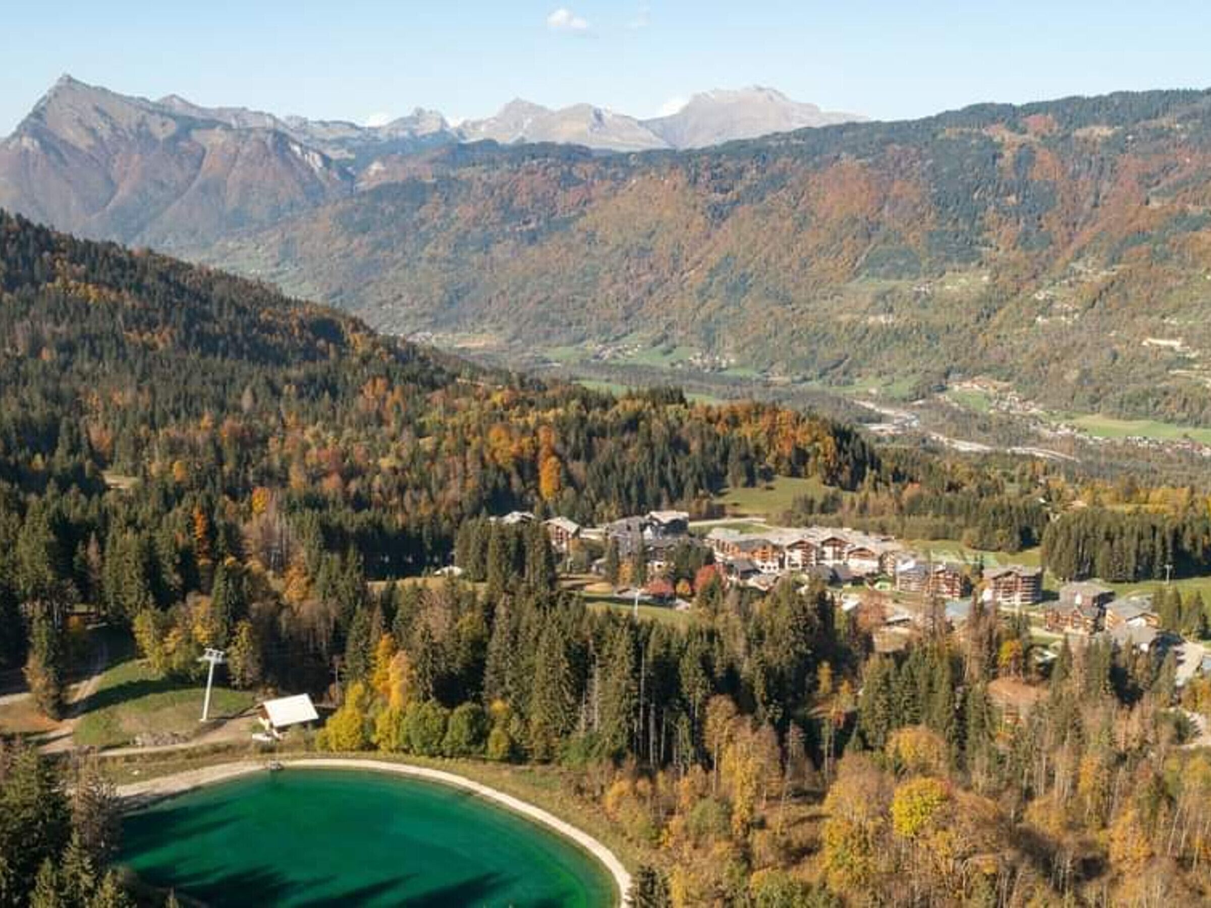 A mountainous landscape with a lake, forested areas, and a cluster of buildings likely serving as a hotel or resort.