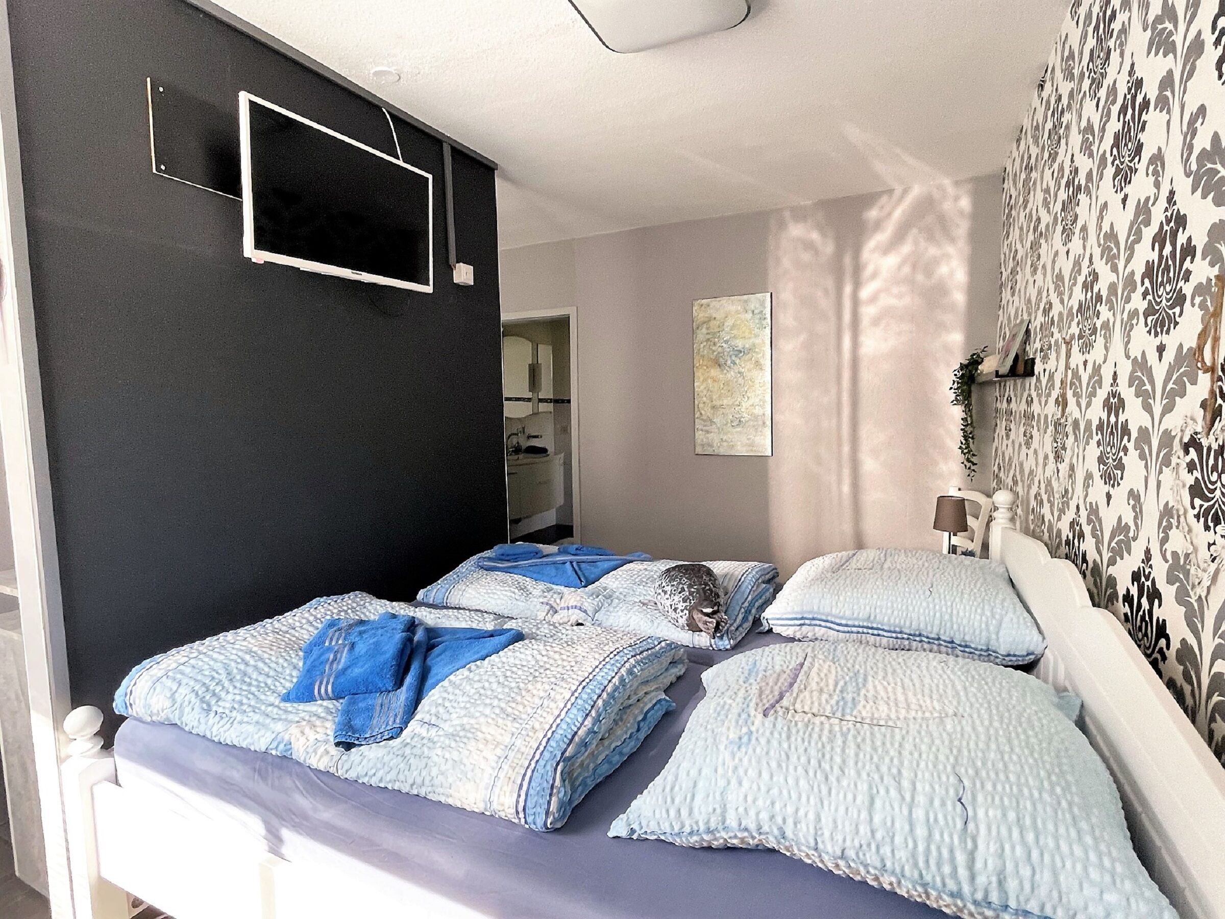 A bedroom with two beds, a TV mounted on the wall, and a bathroom visible through an open door.