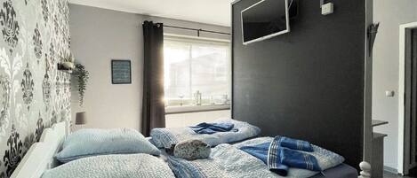Un dormitorio con dos camas, un televisor montado en la pared y una ventana con persianas.