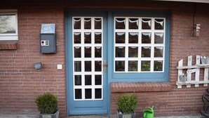 Un edificio de ladrillo con puerta azul, ventanas, un buzón y dos macetas.
