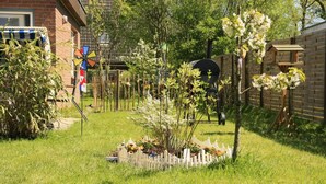 Un jardín con cerca blanca de piquetes, diversas plantas y un molino.